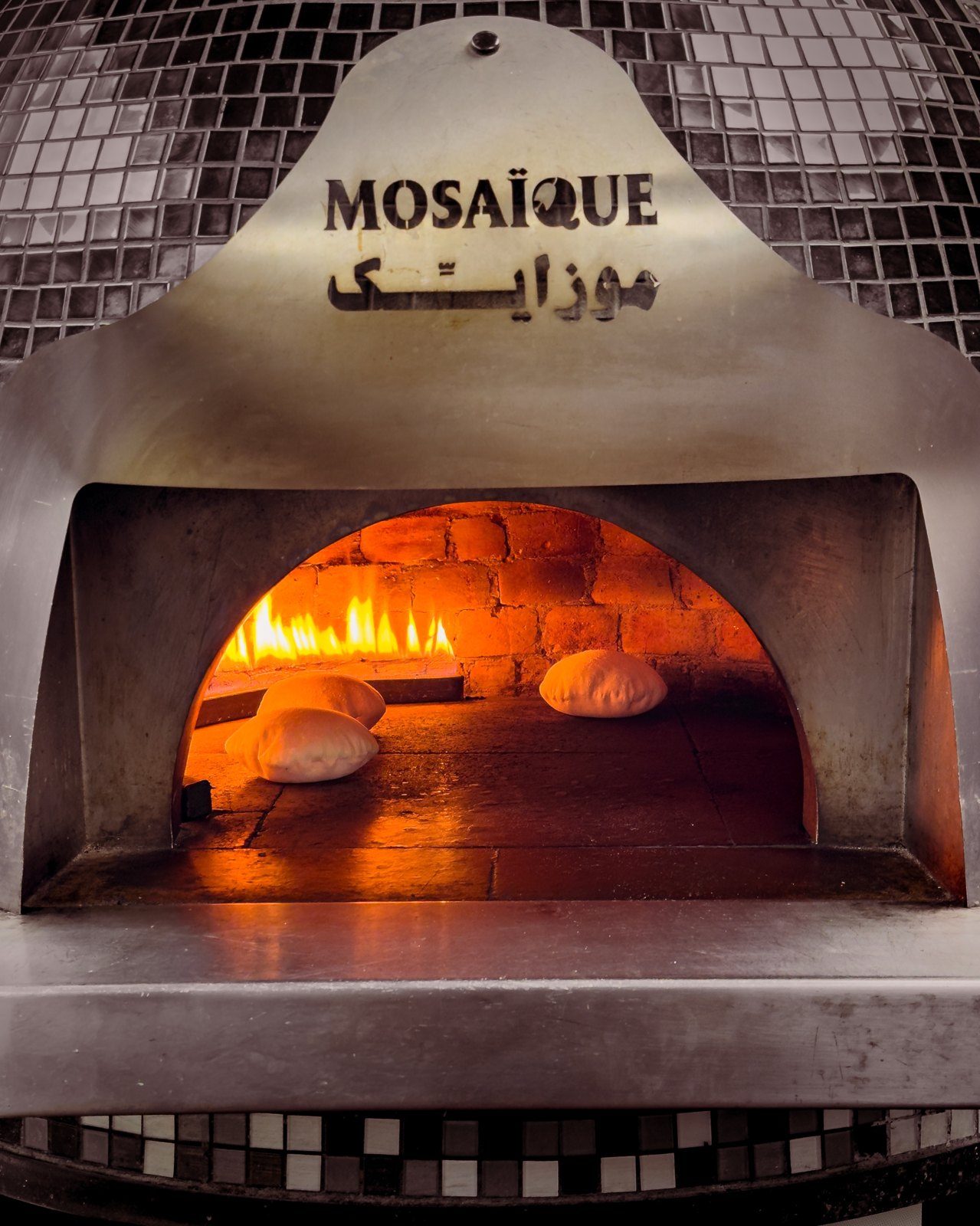 The mosaic-clad bread oven with a live fire and fresh pita inside