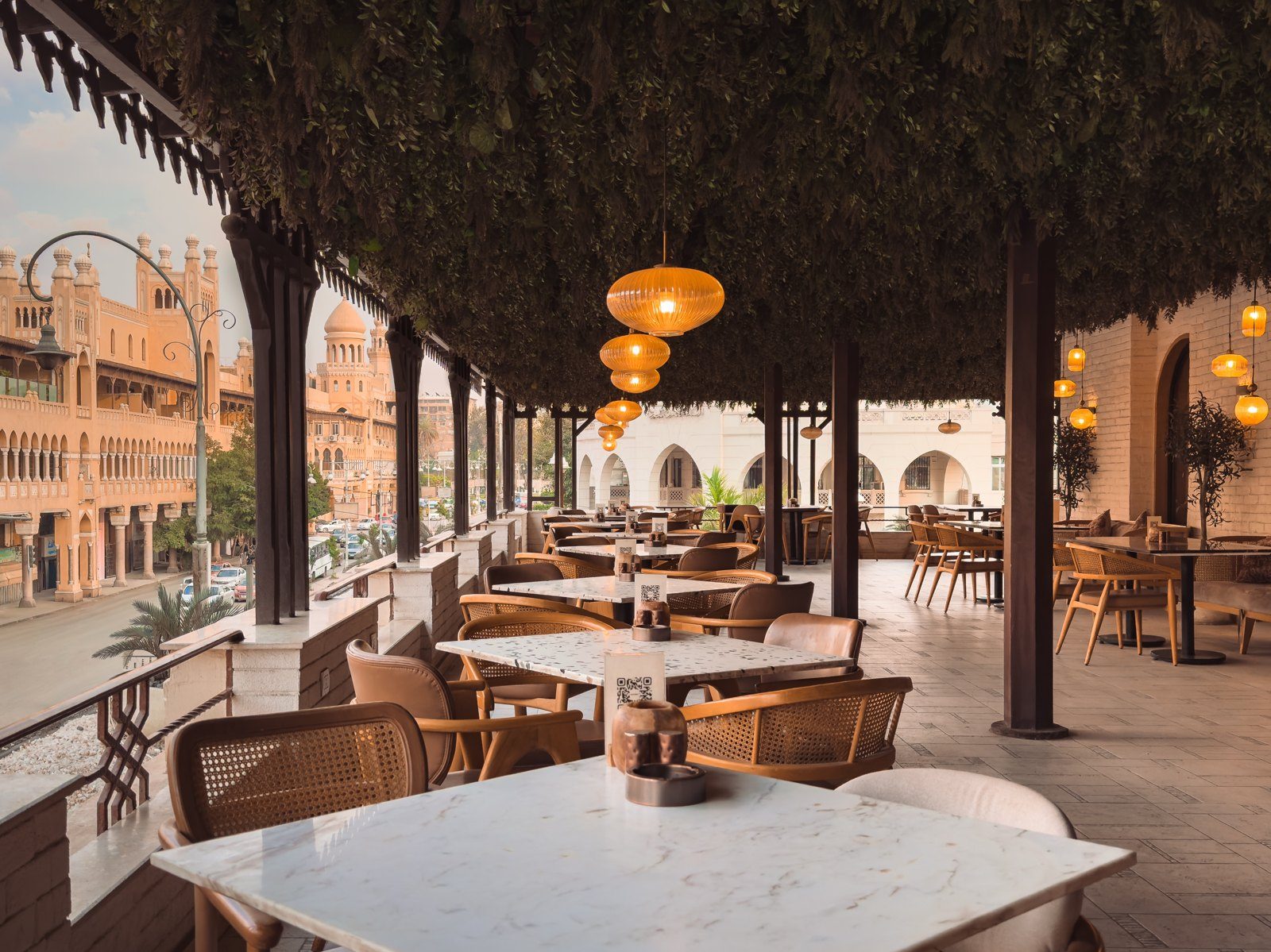 The rooftop terrace at Mosaïque under a canopy of trees, with white marble tables, cane chairs and Korba rooftops beyond